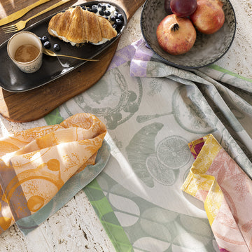 Le Jacquard Francais Brunch Gourmand Kiwi tea towel on table with breakfast foods and other tea towels.